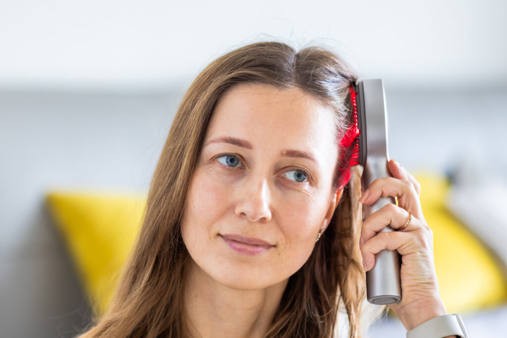 A young woman using red light therapy device on her hair.
