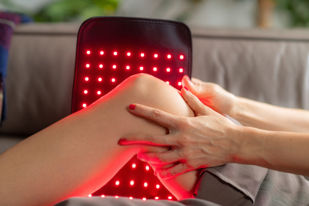 Woman applying a red light therapy pad to her knee, demonstrating what red light therapy does to your body at the cellular level.