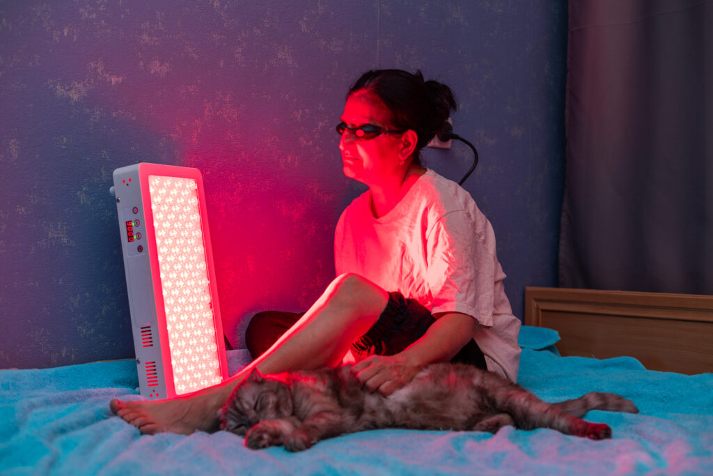 Woman using red light therapy before bed with her cat.
