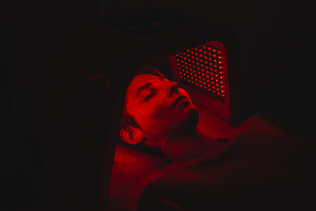 Close-up of red light therapy panel treatment illuminating skin in a dim red glow.