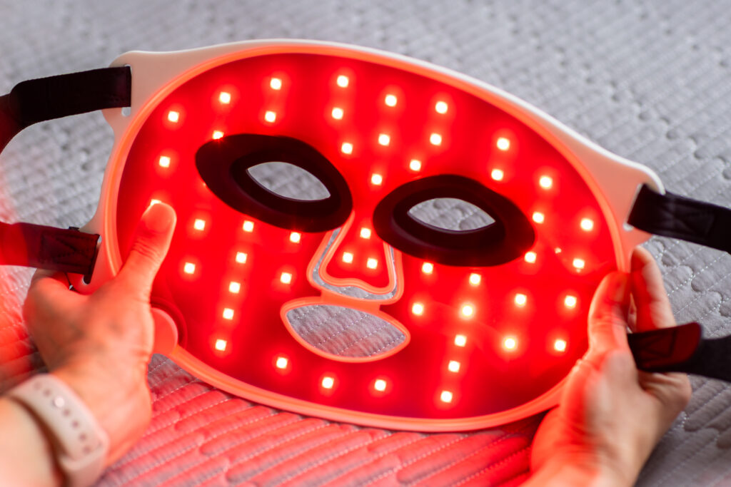 Close-up of hands holding a glowing red LED facial mask, showing how red light therapy for skin works with targeted light panels.