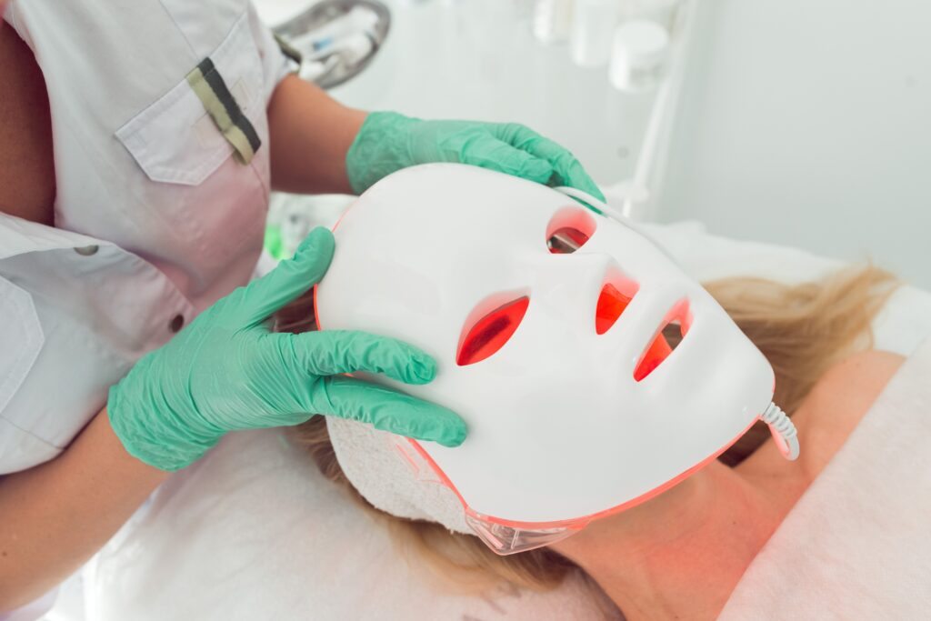 Esthetician applying professional red light therapy for skin using an LED face mask